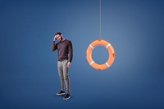 A Bearded Man In Glasses Stands With His Hand On His Forehead Near An Orange Lifebuoy Hanging From A Rope.