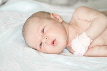 Closeup portrait of cute newborn baby lying down in the bed at home, smiling face, happy childhood, new life concept
