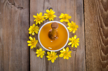 honey in the glass bowl, dipper and yellow flowers around it on wooden background