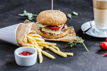 Fast food hamburger (cheeseburger) and french fries with tomato souce on a black table