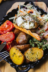 Hot assorted meats, bacon, meat sausages with roasted tomatoes, potatoes, poached egg and fresh cabbage on a platter  