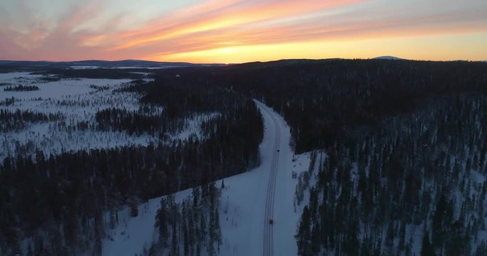 drone shot, following a vehicle, on a frozen route, between finnish woods and polar wilderness, in Pallas-yllastunturi national park, at the arctic circle, at sunset, on a sunny, winter evening dus