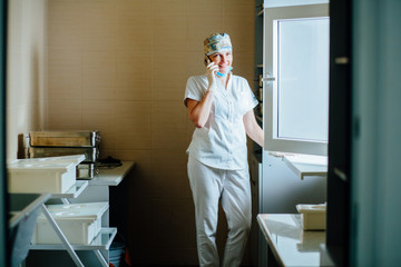 Fototapeta premium Female Surgeon Doctor Talking On Phone In Hospital Room For Equipment . Surgeon medic relaxing after for medical procedure