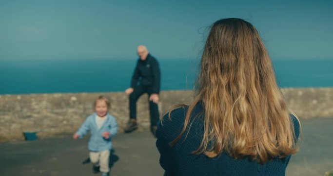 Little toddler running from his grandfather to his mother on the coast