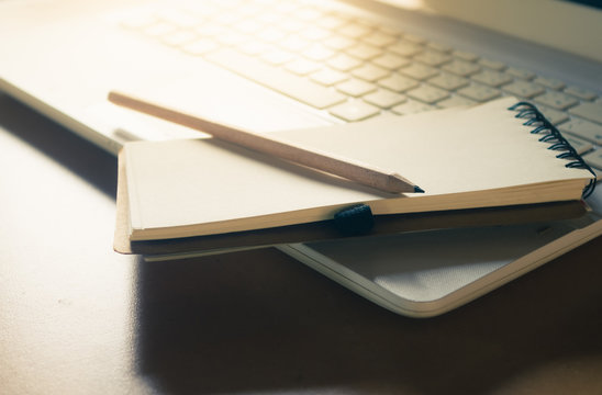 notebook and pencil place on laptop keyboard with morning light, vintage color effect