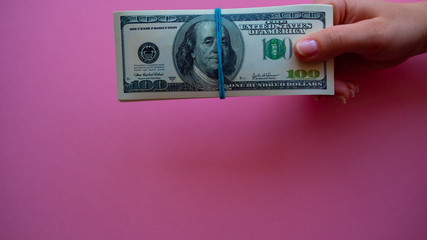 female hand holding money dollars on pink background