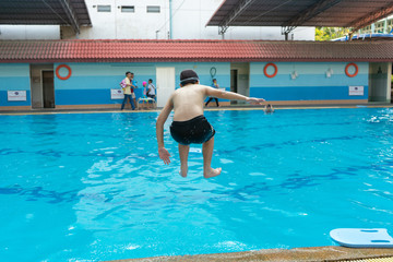 Back portrait of cheerful boy jumping into the swimming pool