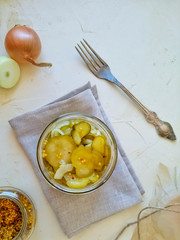 Pickle salad with onions and mustard seeds in an open jar. Near a fork, bulbs and a jar of mustard, on a light background top view.