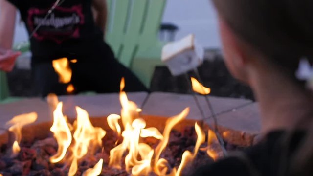 HEBER, UNITED STATES - 02/14/2019: 2 Girl Kids Are Roasting Marshmallow On Open Flame With The Sticks. Hand held shot from behind shoulder of a girl as she and he friend are tasting white marshmallow 