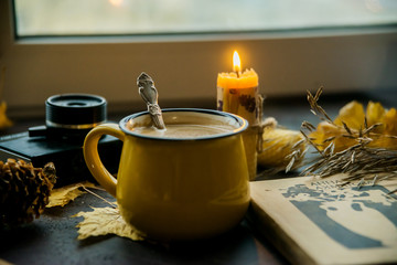 Yellow mug with autumn leaves, a book and candles. The concept of comfort and warmth.