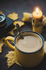 Yellow mug with autumn leaves, a book and candles. The concept of comfort and warmth.