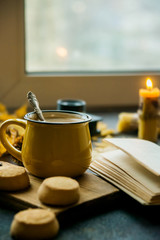 Yellow mug with autumn leaves, a book and candles. The concept of comfort and warmth.