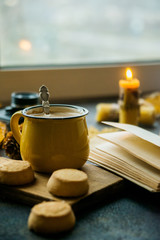 Yellow mug with autumn leaves, a book and candles. The concept of comfort and warmth.