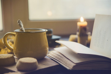 Yellow mug with autumn leaves, a book and candles. The concept of comfort and warmth.