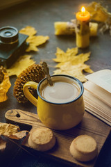 Yellow mug with autumn leaves, a book and candles. The concept of comfort and warmth.