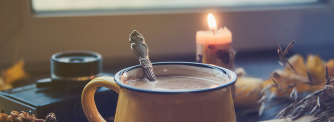Yellow mug with autumn leaves, a book and candles. The concept of comfort and warmth. Banner, long.
