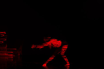 Beautiful dancer moving her body in front of and red light while performing a perfect dance composition of moves. The dance scene is showing off the inferno in a spectacular way, long exposure motion