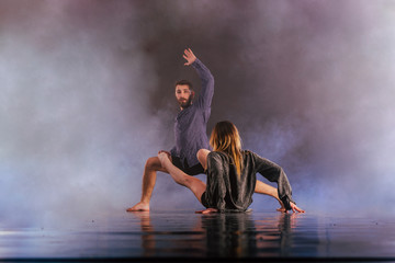 Shoeless dance couple performing multiple unique dance moves in front of a black background surrounded by a lot of smoke.
