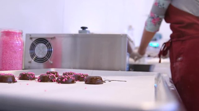 Woman Adds Marshmallow Covered With Liquid Chocolate To A Tray. Close up shot as confectioner puts chocolate marshmellow donuts into a tray with paper towel in the professional kitchen.