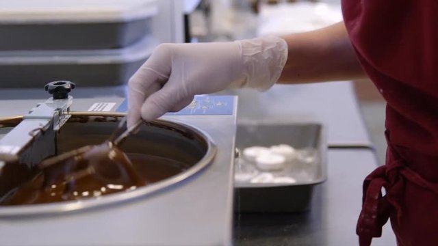 Woman Sinks Marshmallow Donut Onto A Bowl With Liquid Chocolate. Hand held tracking shot as cook sinks white marshmallow into apparatus with liquid chocolate