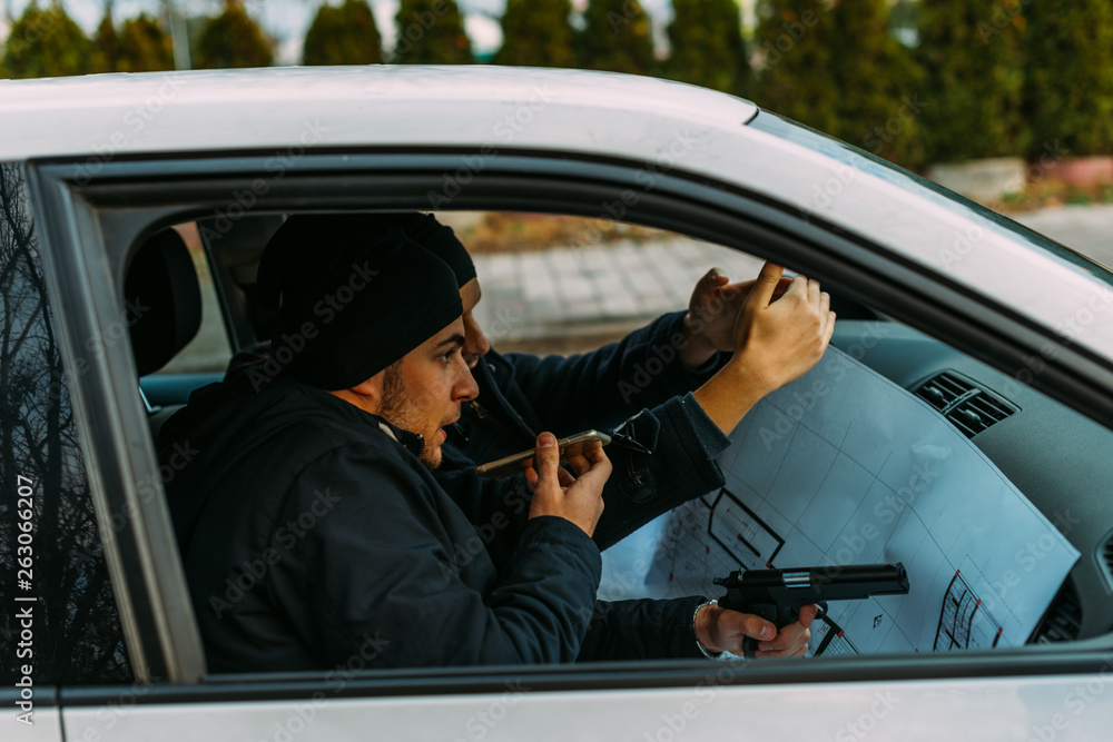 Wall mural Two Thieves parked in an ally waiting while talking on the phone, observing their target and loading their guns.