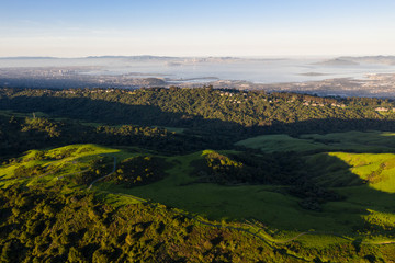 Morning light illuminates the hills surrounding San Francisco Bay. A wet winter has caused lush vegetation growth in the East Bay hills near Oakland and Berkeley. 