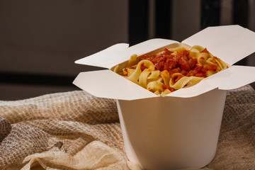 Homemade Pasta, Noodles, fettuccine Alfredo or Bolognese for take away in a white box on a wooden background close up shot. place for logo or copy paste text