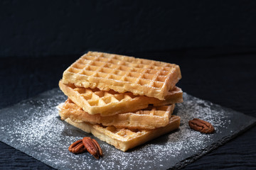 Sweet tasty Belgian waffles close-up, sprinkled with powdered sugar, pecan nuts