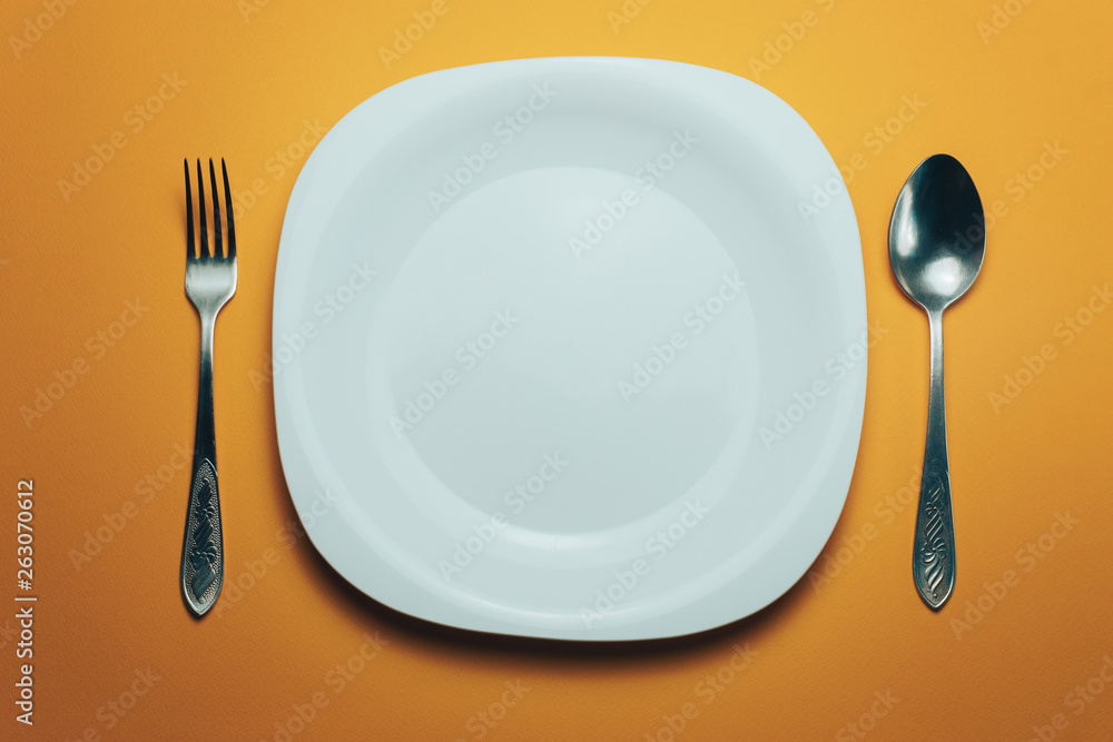 Poster white bowl and a fork with a spoon on an orange background