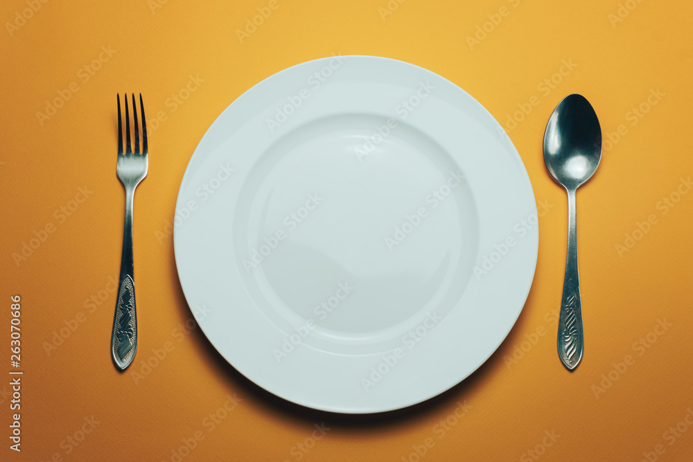 Poster white bowl and a fork with a spoon on an orange background