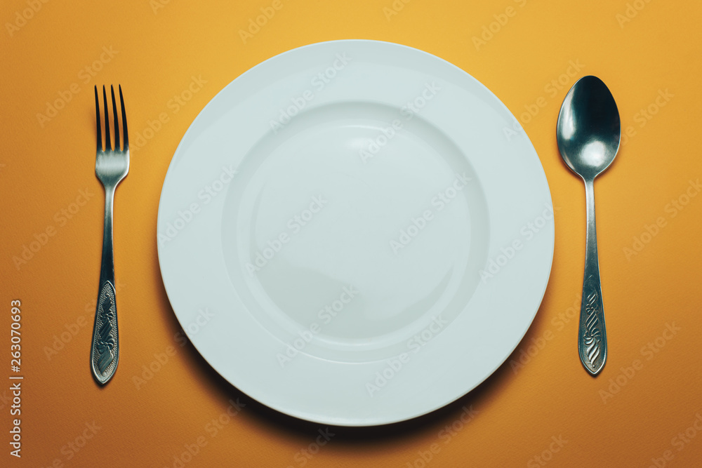 Poster white bowl and a fork with a spoon on an orange background