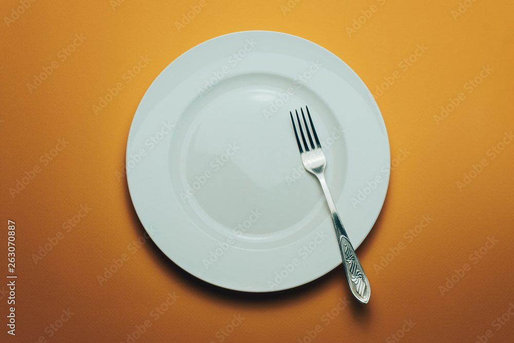 Poster white bowl and a fork with a spoon on an orange background