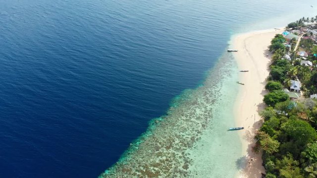 Aerial: flying over tropical Hatta island white sand beach Banda Islands Maluku Indonesia lush green forest turquoise water coral reef scenic travel destination. Color grading version