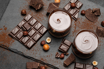 glass bowl of chocolate cream or melted chocolate, pieces of chocolate and hazelnuts on dark concrete background