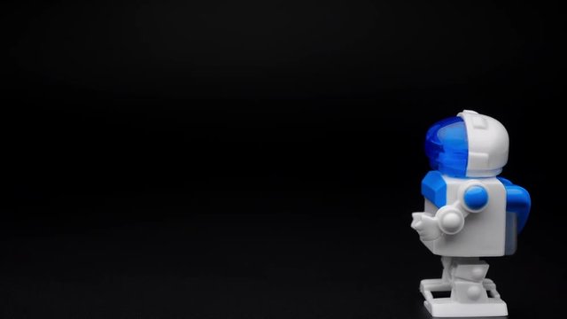 Closeup of white clockwork robot make steps on black background.