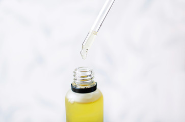 Oily yellow drop falls from cosmetic pipette on white background