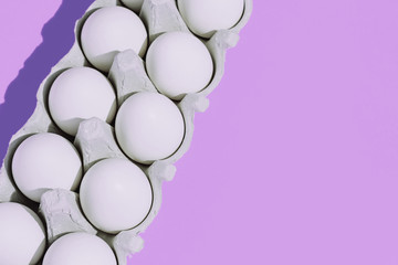 White chicken eggs in a cardboard package with empty space, on a blue background