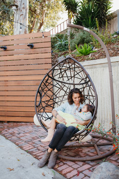 Happy mother talking with daughter sitting on swing seat in yard
