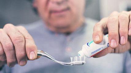 Man extrude a toothpaste from a tube on a toothbrush