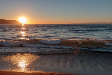 Wet sand foreground and approaching waves at sunset