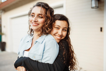 Portrait of smiling daughter embracing mother while standing against house in yard