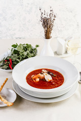 Delicious tomato clam chowder soup with shellfish, shrimps, squid, mussels, octopus and seafood close-up on a in a white bowl on the  on a served white table