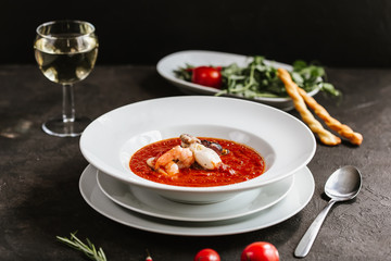 Delicious tomato clam chowder soup with shellfish, shrimps, squid, mussels, octopus and seafood close-up on a in a white bowl on the served black table