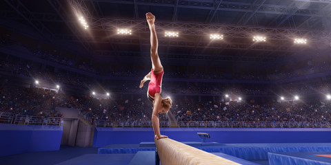 Female athlete doing a complicated exciting trick on gymnastics balance beam in a professional gym....