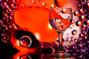 transparent glass with water and oily drops on purple background 