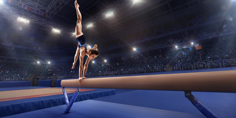 Female athlete doing a complicated exciting trick on gymnastics balance beam in a professional gym. Girl perform stunt in bright sports clothes - obrazy, fototapety, plakaty