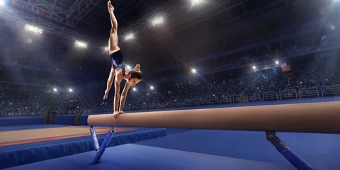  Female athlete doing a complicated exciting trick on gymnastics balance beam in a professional gym. Girl perform stunt in bright sports clothes © Alex