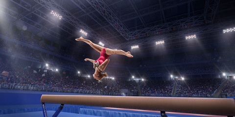 Fototapeta na wymiar Female athlete doing a complicated exciting trick on gymnastics balance beam in a professional gym. Girl perform stunt in bright sports clothes