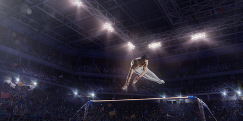 Fototapeta na wymiar Male athlete doing a complicated exciting trick on horizontal gymnastics bars in a professional gym. Man perform stunt in bright sports clothes