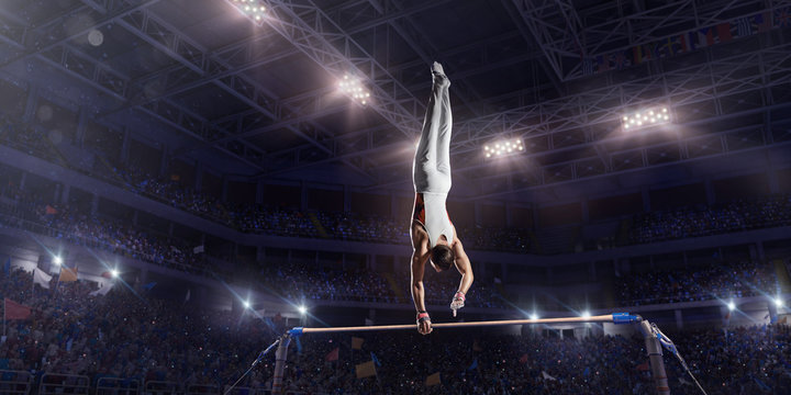 Male athlete doing a complicated exciting trick on horizontal gymnastics bars in a professional gym. Man perform stunt in bright sports clothes